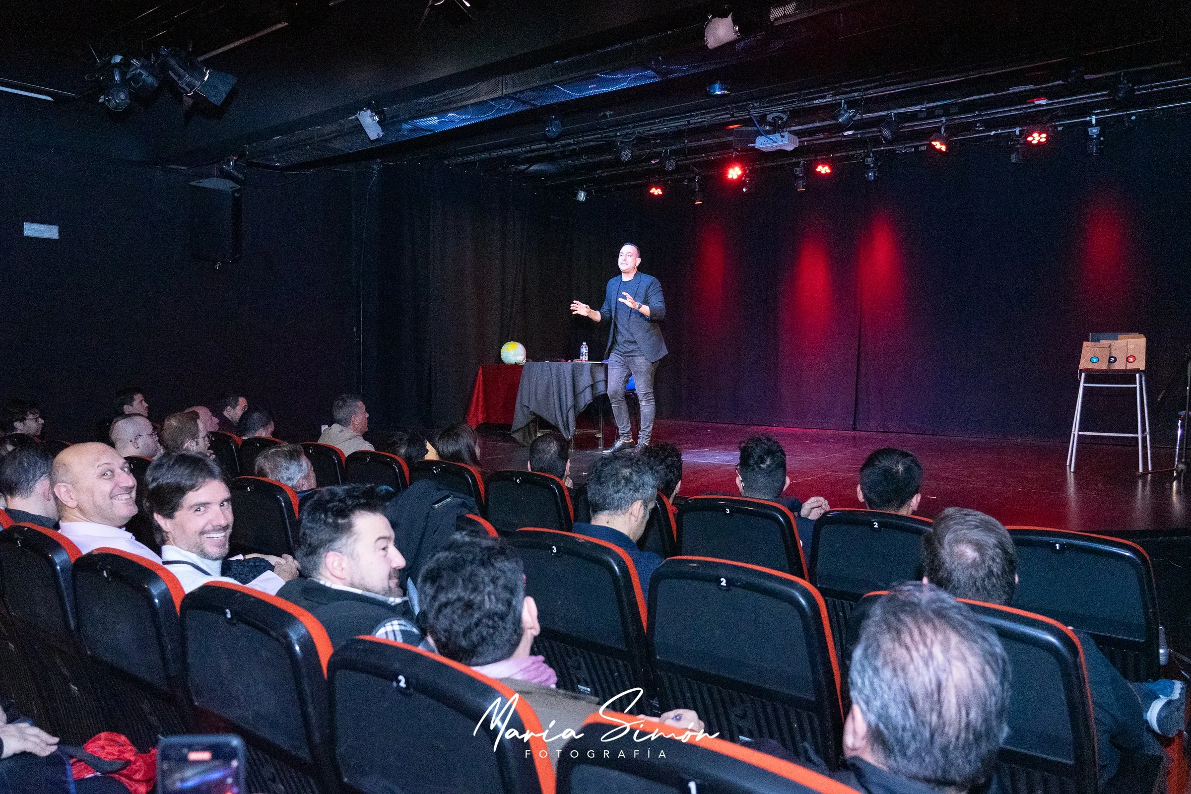 Larry en el escenario de una sala chica, con el público en primer plano