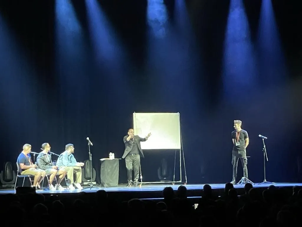 Larry en un teatro, con voluntarios sentados y una pizarra